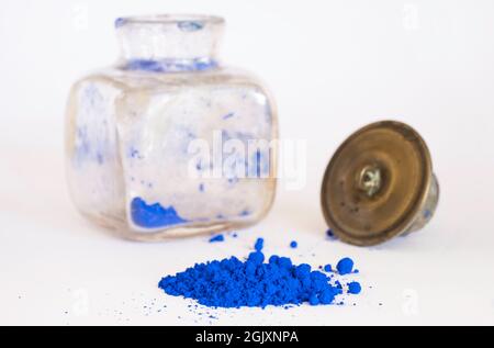 Blaues Pigment mit verschwommenem antikem quadratischem Glasfläschchen mit Kupferstopfen im Hintergrund. Das Pigment wird mit Leinöl gemischt, um Ölfarbe zu erhalten Stockfoto
