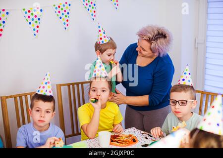 Unterstützende Mutter hilft kleinen Jungen, Party-Horn zu blasen Stockfoto