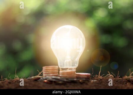 Stapel von Münzen und Geld mit Glühbirne Energiesparkonzept. Einsparungs-, Buchhaltungs- und Finanzkonzept. Stockfoto