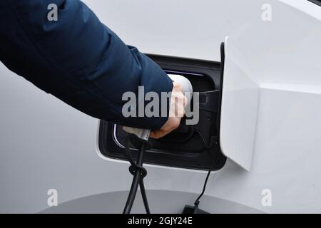 Ein Mann, der Ladegerät in sein weißes Elektroauto setzt Stockfoto