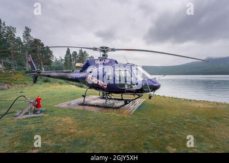 Vietas, Schweden - 08.16.2021: Kleiner blauer Fiskflyg-Hubschrauber, der bei schlechtem Wetter auf einem Holzbrett am See im Stora Sjofallet Nationalpark sitzt. Stockfoto