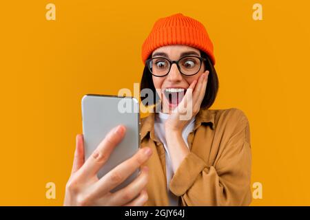 Omm. Überrascht Hipster Frau Blick auf Smartphone-Bildschirm, emotional reagiert auf gute Nachrichten, gelber Hintergrund Stockfoto