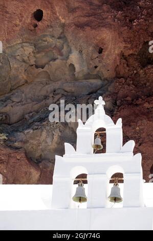 Weißer Glockenturm der orthodoxen Kirche St. Nikolaus am Fuße des Felsens in der Nähe des roten Strandes auf der Insel Santorini. Stockfoto