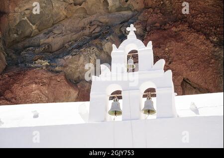 Weißer Glockenturm der orthodoxen Kirche St. Nikolaus am Fuße des Felsens in der Nähe des roten Strandes auf der Insel Santorini. Stockfoto
