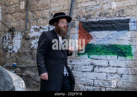 Ein orthodoxer Jude kommt an einer palästinensischen Flagge vorbei, die von extremen antizionistischen Haredi-Juden in Mea Shearim, einer ultra-orthodoxen Enklave in West-Jerusalem Israel, auf eine Wand gesprüht wurde Stockfoto