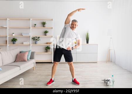 Aktiver Lebensstil. Reifer Mann macht Flexibilitätsübungen für ein gesünderes Leben, arbeitet zu Hause, leerer Raum Stockfoto