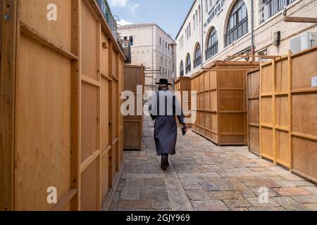 Ein orthodoxer Jude geht an einer Straße vorbei, die voll von traditionellen, temporären Holzhütten ist, die während des einwöchigen jüdischen Festivals von Sukkot oder Sukkkot im Batei Ungarin Haredi-jüdischen Viertel in der Nähe der ultra-orthodoxen Mea Shearim-Enklave in West-Jerusalem Israel gebaut wurden Stockfoto