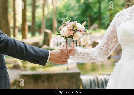 Der Bräutigam reicht der Braut einen Hochzeitsstrauß. Nahaufnahme von frisch vermählten Händen und zartem Bouquet Stockfoto