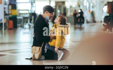 Liebevolle Mutter und Sohn am Flughafen. Mutter in Gesichtsmaske, die ihren Sohn festhält, nachdem sie während einer Pandemie aus dem Ausland angekommen war. Stockfoto