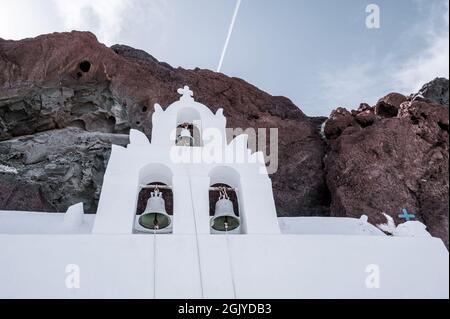Weißer Glockenturm der orthodoxen Kirche St. Nikolaus am Fuße des Felsens in der Nähe des roten Strandes auf der Insel Santorini. Stockfoto