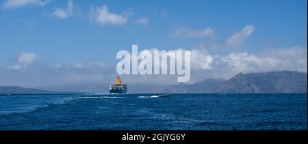 Kleines Boot hinter dem Schiff in der Nähe der Insel Santorini in Aegea Sea, Griechenland. Fähre zum Hafen. Transport auf dem Seeweg. Stockfoto