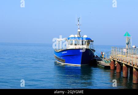 The Needles, Isle of Wight, 2021. Ein leuchtend blaues Boot, das an einem kleinen Anlegesteg festgemacht ist und darauf wartet, Touristen ins Meer zu bringen. Das Boot ist ein altes Fischerboot Stockfoto