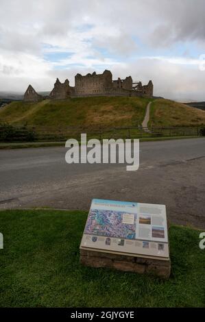 Touristeninformationsschild für Ruthven Barracks mit verschwommenem Hintergrund von Gebäuden. Blauer Himmel und Wolken. Straße und Weg im Blick. Keine Personen. Stockfoto