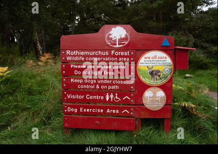 Rot-weißes Schild für den Rothiemurchus-Wald mit Pfeilen zum Besucherzentrum, Hundeübungsbereich. Verschwommener Waldhintergrund. Regeln über Feuer und Hunde. Stockfoto