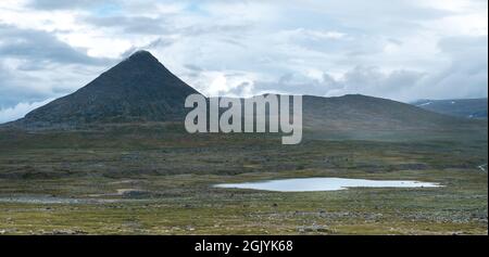 Pyramidenform des Berges Slugga in Schwedisch Lappland mit See vor dem Blick vom Stora Sjofallet Nationalpark an einem bewölkten Tag des arktischen Sommers. Stockfoto