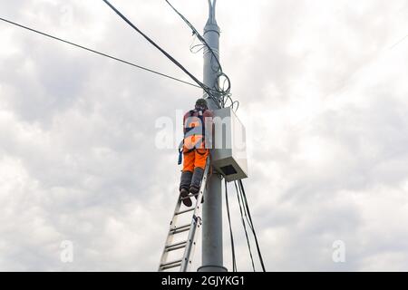 Perm, Russland - 25. August 2021: Elektriker oder Telekommunikationsleiter arbeitet an der Verlegung eines Kabels an der Spitze eines Telefonpols Stockfoto