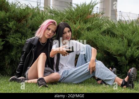 Zwei Teenager-Mädchen beobachten etwas auf einem Smartphone, auf dem Gras hinter den Büschen im Park Stockfoto