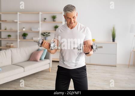 Workout während des Lockdown. Ein sportlicher Mann mittleren Alters, der zu Hause Hanteltraining macht und im Wohnzimmer trainiert Stockfoto