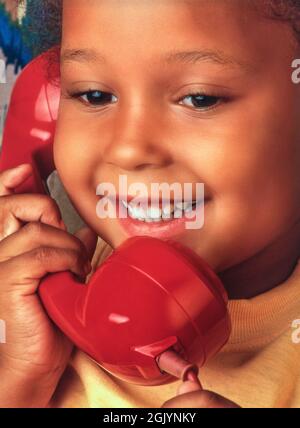 Kleinkind 4 Jahre altes Mädchen African Caribbean ziemlich niedlich glücklich lächelnd Gespräch auf ihrem roten Retro Vintage-Stil Telefon Hörer Stockfoto