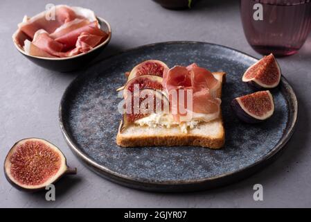 Crostini mit italienischem Schinken und Ricotta, Toast mit Prosciutto und Feigen auf dunklem Grund, Nahaufnahme. Stockfoto