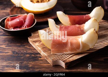 Frische Melonenscheiben mit italienischem Schinken, Prosciutto und Früchtevorspeise auf dunklem Holzhintergrund, Nahaufnahme. Stockfoto