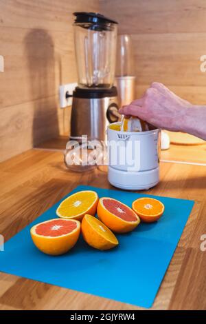 Mann presst Saft aus gehackten roten und orangen Orangen in der Küche aus nächster Nähe auf einem Entsafter Stockfoto