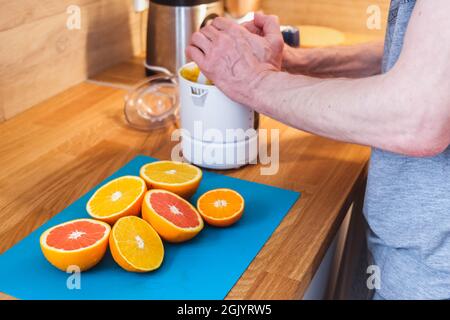 Mann presst Saft aus gehackten roten und orangen Orangen in der Küche aus nächster Nähe auf einem Entsafter Stockfoto