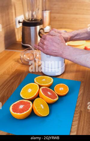 Mann presst Saft aus gehackten roten und orangen Orangen in der Küche aus nächster Nähe auf einem Entsafter Stockfoto