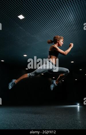 Frau springt hoch in Sportkleidung auf einem schwarzen Hintergrund der Turnhalle. Stockfoto