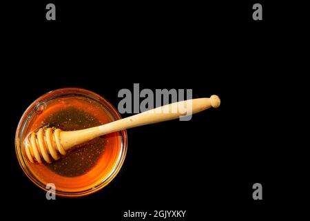 Honig in Schüssel mit Holzstab isoliert auf schwarzem Grund. Stockfoto