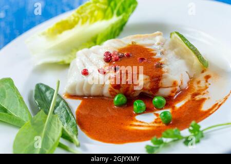 Gedünstetes Kabeljaufilet mit Paprikasoße und Salatblättern. Stockfoto