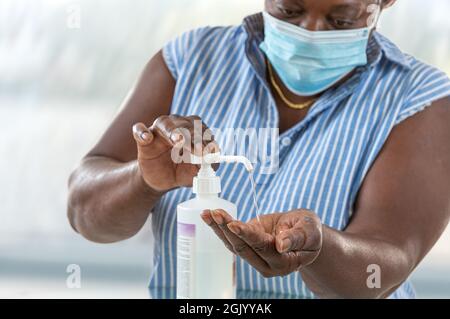 Coronavirus. Geschäftsfrau, die von zu Hause aus mit einer Schutzmaske zum Tragen einer Schutzmaske arbeitet. Reinigen ihrer Hände mit Desinfektionsmittel-Gel. Stockfoto