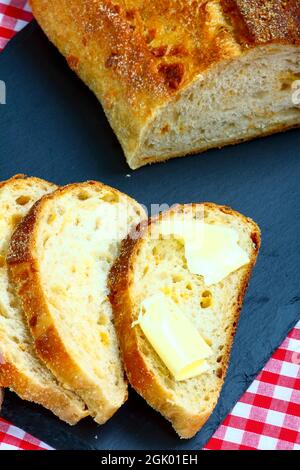 Frisch gebackener Sauerteig und Käse handwerkliches Brot mit gebutterten Brotscheiben, die geschnitten und auf eine Schieferplatte gelegt wurden Stockfoto