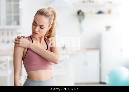 Traurige kaukasische junge blonde Dame, die nach dem Training zu Hause an Verletzungen und Schulterschmerzen leidet Stockfoto