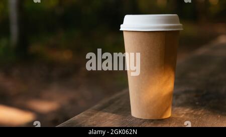 Kleine leere Pappbecher zum Mitnehmen auf der Bank im Wald. Nahaufnahme. Wandern mit heißem Getränk. Stockfoto