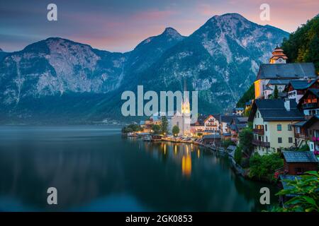 Hallstatt, Österreich - Eine malerische Postkartenansicht des berühmten Dorfes Hallstatt, die sich in der Abenddämmerung am Hallstattersee in den österreichischen Alpen widerspiegelt. Stockfoto