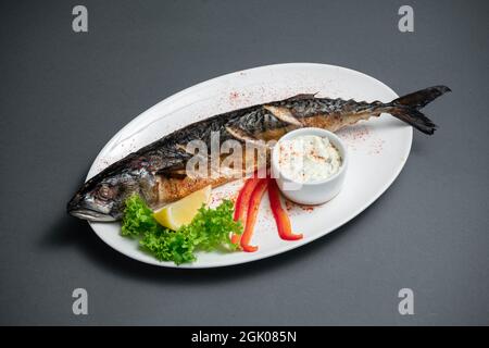 Nahaufnahme von gebackenem Makrelenfisch mit Sauce auf weißem Teller auf schwarzem Hintergrund Stockfoto