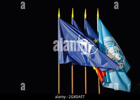 Otopeni, Rumänien - 9. September 2021: NATO, Rumänien, Europäische Union und UNO-Flaggen im Wind in der Nacht. Stockfoto