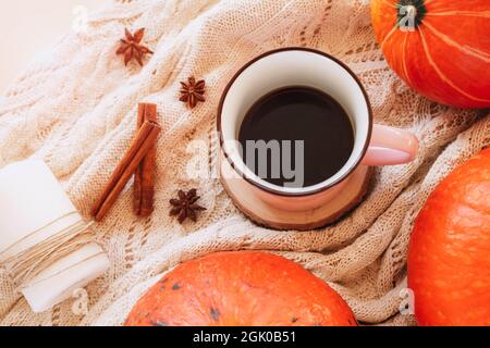 Eine Tasse Kaffee auf dem Tisch mit Kürbissen, Sternanise und Zimtstangen auf einem Strickpullover. Herbstkonzept, Draufsicht. Stockfoto