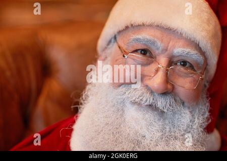 Porträt des lächelnden freundlichen Weihnachtsmanns mit weißem Bart und Augenbrauen, die Brillen und Mütze tragen Stockfoto