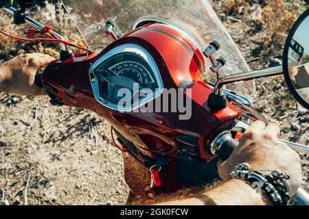 Die Hände des Mannes am Lenkrad, der Moped oder Scooter fährt, Nahaufnahme. Fahrer fährt Retro rot Motorrad. Lenker des Motorrads. Stockfoto