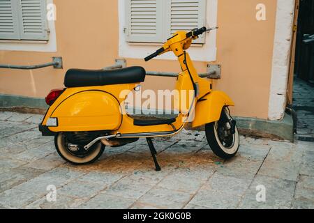 Gelber Retro-Roller auf einer Stufe in der Nähe des alten Gebäudes. Schönes Vintage-Design von Motorrad. Stockfoto