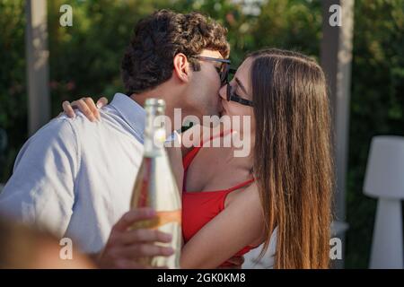 Junges Paar küsst sich im Terrassengarten mit einer Sekt-Flasche. Stockfoto