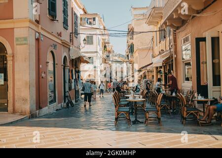 Korfu, Griechenland - September 2021. Schöne gemütliche schmale Straße in der alten griechischen Stadt. Historisches europäisches Zentrum mit Café und Menschen, Touristen. Stadtbild Stockfoto