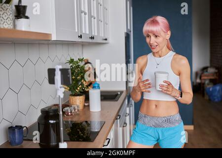 Junge Frau zeigt Glas Nahrungsergänzungsmittel Aufnahme neuer Video in der Küche Stockfoto