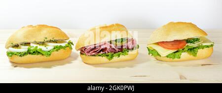 Dreireihige Sandwichrollen mit Ei, Salami und Käse auf einem Holztisch vor hellem Hintergrund, Panoramafotor, ausgewählter Fokus, enge Tiefe o Stockfoto