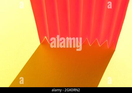 Rosa gefaltetes Papier gegen Sonnenlicht auf gelbem Hintergrund. Geometrische Formen und Linien. Minimalistischer Hintergrund. Speicherplatz kopieren. Stockfoto