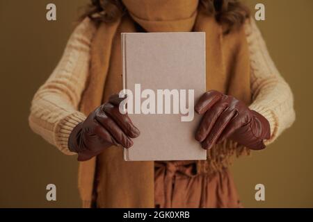 Hallo Herbst. Nahaufnahme einer Frau mittleren Alters mit Buch und Lederhandschuhen vor bronzefarbenem Hintergrund. Stockfoto