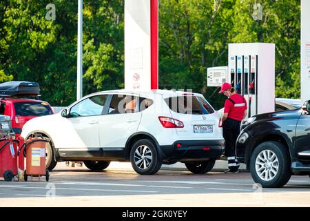Woronesch. Russland. 23. Juli 2021. Ein weiblicher Tanker in roter Uniform füllt den Tank einer weißen Kreuzung an einer Tankstelle auf. Stockfoto