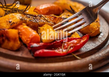 Essen gegrillter Kürbis und Gemüse. Nahaufgabel in gerösteten Lebensmitteln auf Holzplatte Stockfoto